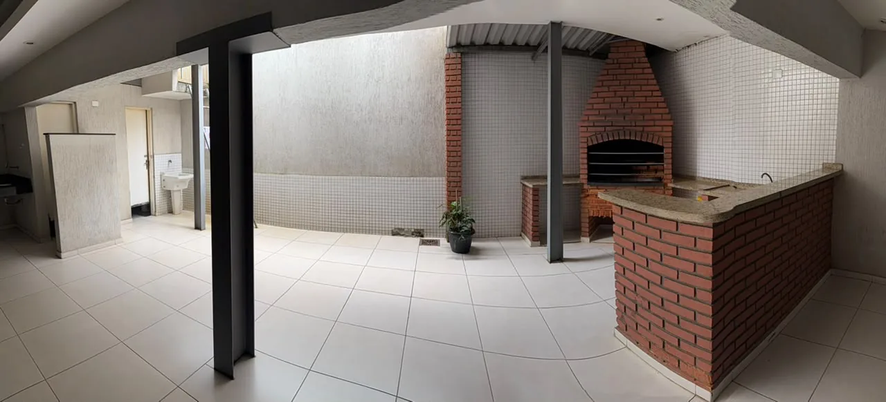 Área embaixo do salão com churrasqueira de tijolo, bancada de granito e piso claro