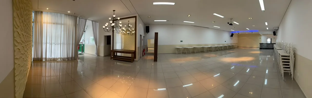 Salão vazio visto de ponta a ponta, com lustre, cortinas e piso claro espelhado